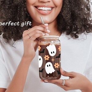 May include: A glass jar with a brown lid and a black and white ghost pattern. The jar is filled with a dark liquid and has a straw sticking out of it.