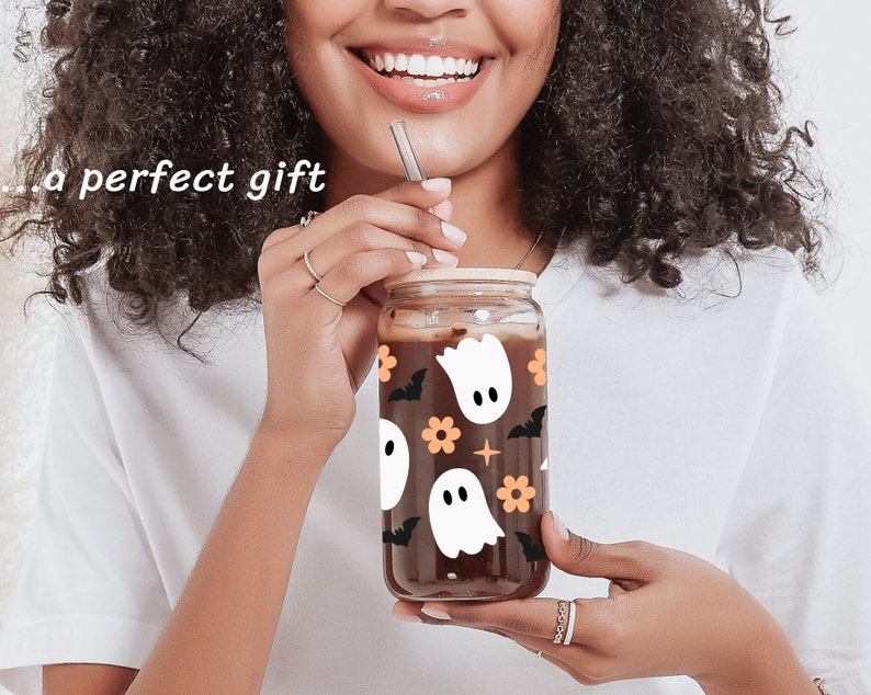 May include: A glass jar with a brown lid and a black and white ghost pattern. The jar is filled with a dark liquid and has a straw sticking out of it.