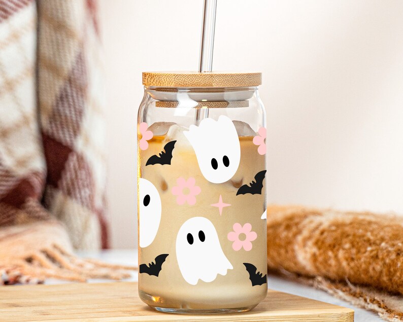 May include: A glass jar with a bamboo lid and a straw filled with a light brown beverage. The jar has a Halloween-themed design with white ghosts, black bats, and pink flowers.