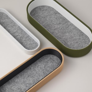 May include: Three oval-shaped storage containers with a grey felt lining. The containers are made of different materials: white, beige, and green.
