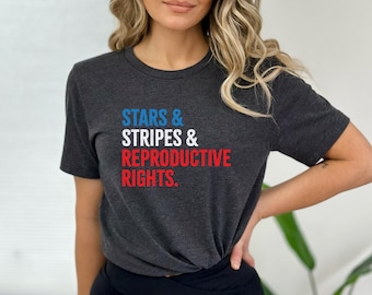 Könnte beinhalten: Dunkelgraues T-Shirt mit dem Text "STARS & STRIPES & REPRODUCTIVE RIGHTS" in Blau, Weiß und Rot. Das Shirt hat kurze Ärmel und einen Rundhalsausschnitt.