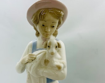 May include: A porcelain figurine of a girl wearing a pink hat and a blue dress, holding a white lamb in her arms.