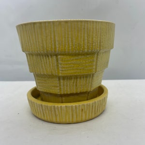 May include: A yellow ceramic planter with a geometric design and a matching saucer. The planter has a crackled glaze and a ribbed texture.