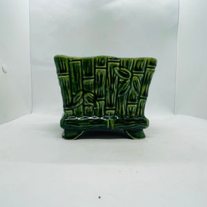 Puede incluir: Una maceta de cerámica verde con un diseño de bambú. La maceta tiene cuatro pequeñas patas y es perfecta para plantas pequeñas.