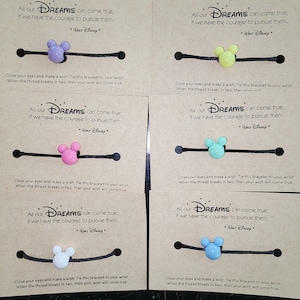May include: Six cards with a black elastic bracelet with a Mickey Mouse charm. Each card has a different colored charm: purple, yellow, pink, blue, white, and light blue. The cards all have the same text: "All our DREAMS can come true, if we have the courage to pursue them. *Walt Disney*" and instructions to tie the bracelet to your wrist and make a wish. The thread will break in two, and your wish will come true.