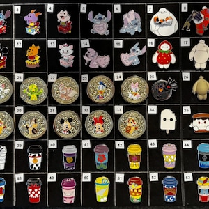 May include: A collection of Disney-themed pins and coffee cup-shaped pins. The pins feature various characters like Stitch, Mickey Mouse, and Baymax. The coffee cup pins have colorful designs. The items are arranged on a black display board.