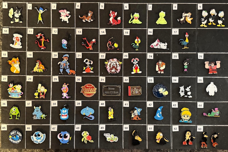 May include: A collection of colorful character charms, including cartoon figures like Simba, Baymax, and Genie. The charms are arranged on a black surface, showcasing a variety of designs and colors. These charms are likely for shoes or bracelets.