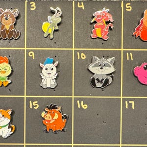 May include: A collection of colorful cartoon character charms, including a white dog, a brown bear, a green rabbit, a red dragon, a red lobster, and a tan creature. Other charms include a monkey, a chick, a goat, a raccoon, a pink frog, and a cat.
