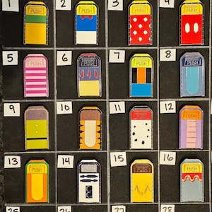 May include: A collection of 16 colorful enamel pins, each featuring a rectangular design with a yellow top and the word "PUSH". The pins showcase various patterns and designs, including stripes, polka dots, and character-inspired motifs.