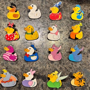 May include: A collection of 16 rubber duck pins featuring various Disney characters. The ducks are in a variety of colors, including yellow, red, blue, green, pink, and purple. Some of the characters include Mickey Mouse, Donald Duck, Goofy, and Tinkerbell.