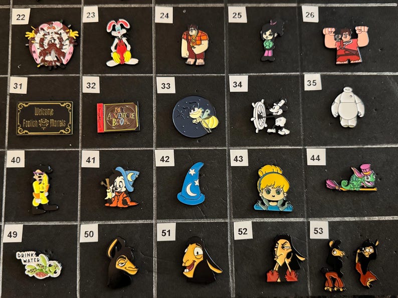 May include: A collection of colorful enamel pins featuring various cartoon characters and themed designs. Includes pins of a rabbit, a wizard hat, a book, and characters from animated films. The pins are arranged on a black surface.