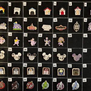 May include: A collection of Disney-themed enamel pins, including house-shaped pins, character pins, and pins featuring the Avengers logo. The pins are arranged on a black surface.