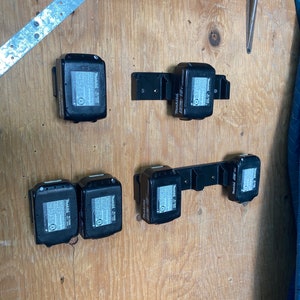 Peut inclure: Six batteries noires pour outils électriques sont montées sur un mur en bois. Les batteries sont étiquetées "DeWalt 20V MAX".