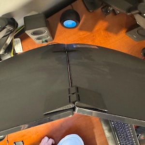 Puede incluir: Vista superior de un escritorio de computadora con dos monitores de computadora negros curvos grandes. El escritorio es de madera y tiene varios accesorios tecnológicos, incluidos altavoces, brazos de monitor y un teclado.