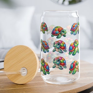 May include: A clear glass reusable water bottle with a bamboo lid and a straw. The bottle is decorated with a colorful pattern of cartoon turtles.