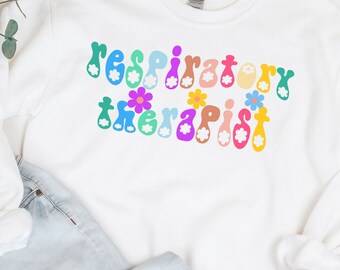 May include: White sweatshirt with the text "respiratory therapist" in rainbow colors with flowers. The sweatshirt is paired with light blue jeans and leopard print flats.