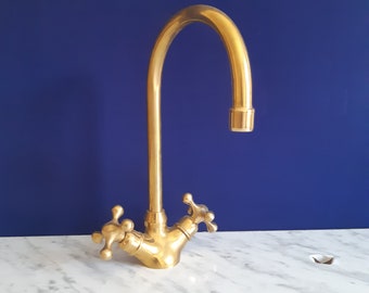 May include: A gold-toned kitchen faucet with a high arc spout and two lever handles. The faucet is mounted on a white marble countertop.