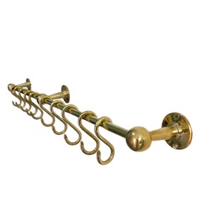 Puede incluir: Un colgador de ollas de latón con un remate redondo y ocho ganchos. El colgador está montado en la pared con una placa redonda.