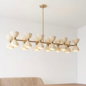 May include: A linear chandelier featuring a long, thin brass-toned metal rod suspended from the ceiling. Attached to the rod are multiple light fixtures, each shaped like a double-ended flower or hourglass with white, petal-like shades.