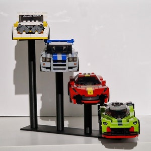 K&ouml;nnte beinhalten: Ein wei&szlig;er, blauer, roter und gr&uuml;ner Lego-Auto-Pr&auml;sentationsst&auml;nder mit vier Autos. Der St&auml;nder hat drei schwarze Metallstangen. Die Autos sind ein wei&szlig;er Audi mit dem Text "Audi Team" auf der Vorderseite, ein blau-wei&szlig;es Auto, ein rotes Auto und ein gr&uuml;nes Auto.