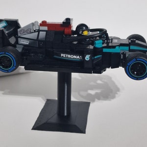 May include: A black and blue Lego Formula 1 race car with the Petronas logo and the number 6 on the side. The car is on a black stand and has a driver figure in the cockpit.