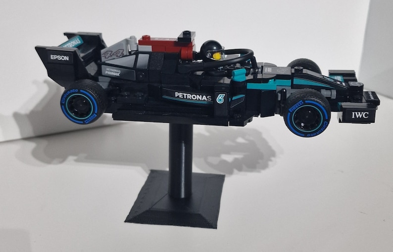 May include: A black and blue Lego Formula 1 race car with the Petronas logo and the number 6 on the side. The car is on a black stand and has a driver figure in the cockpit.