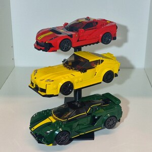 May include: Three Lego car models on a black display stand. The top car is red, the middle car is yellow, and the bottom car is green.