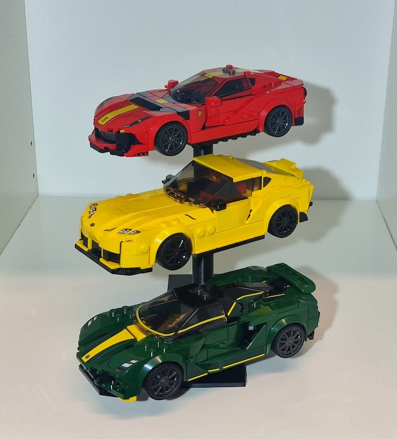 May include: Three Lego car models on a black display stand. The top car is red, the middle car is yellow, and the bottom car is green.