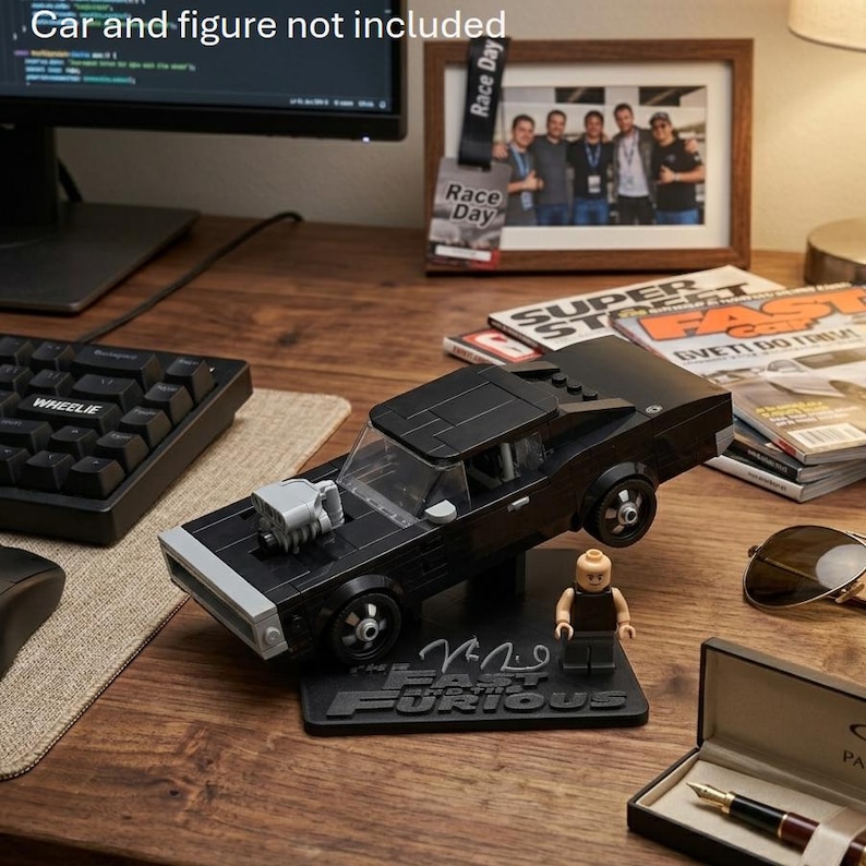 May include: A black plastic building block model of a muscle car featuring a prominent grey engine block protruding from the hood, mounted on a black display stand with the text Fast and the Furious, accompanied by a small plastic figure.