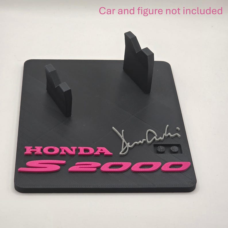 May include: A black rectangular display stand featuring two upright supports, pink raised lettering reading HONDA S2000, and a grey signature. The text Car and figure not included is printed in pink at the top of the image.