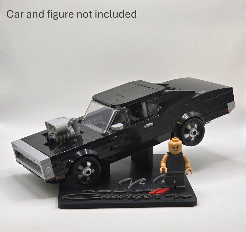 May include: A black building block model of a Dodge Charger car with a grey engine protruding from the hood, mounted on a black display stand with the text Dodge Charger R/T. A small plastic figure stands on the base. Car and figure not included.