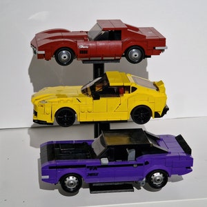 May include: Three toy cars on a stand. The top car is red, the middle car is yellow, and the bottom car is purple.