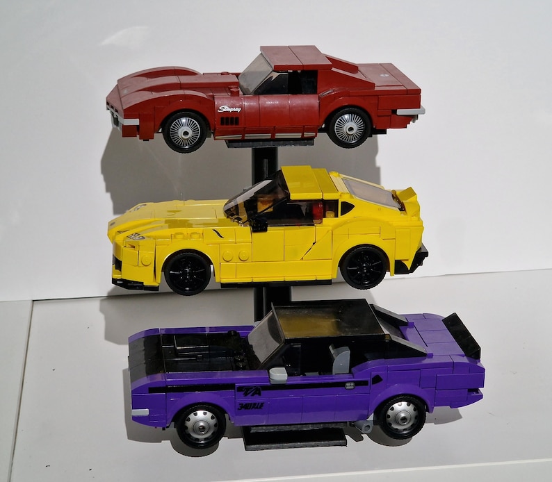 May include: Three toy cars on a stand. The top car is red, the middle car is yellow, and the bottom car is purple.