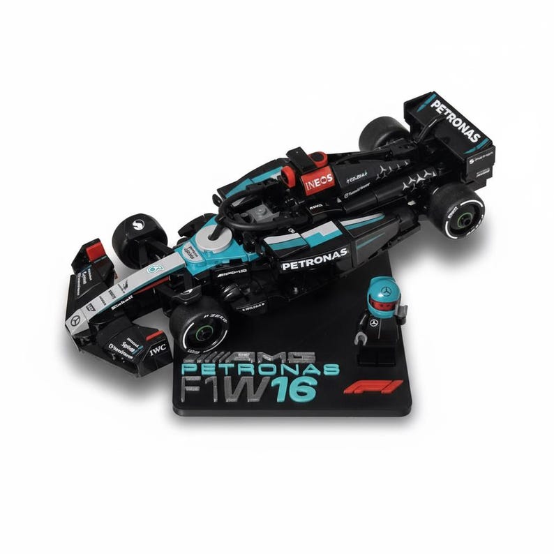May include: A black and teal Formula 1 race car model with the word "PETRONAS" on the side. The model includes a small figure of a driver and sits on a black base with the text "AMG PETRONAS F1 W16".