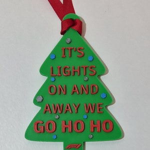 Puede incluir: Adorno de &aacute;rbol de Navidad verde con texto rojo "IT'S LIGHTS ON AND AWAY WE GO HO HO HO". Tiene una cinta roja para colgar y est&aacute; decorado con detalles azules y plateados. Decoraci&oacute;n festiva navide&ntilde;a.