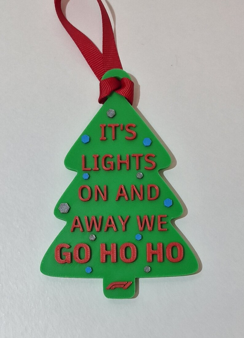 Puede incluir: Adorno de &aacute;rbol de Navidad verde con texto rojo "IT'S LIGHTS ON AND AWAY WE GO HO HO HO". Tiene una cinta roja para colgar y est&aacute; decorado con detalles azules y plateados. Decoraci&oacute;n festiva navide&ntilde;a.