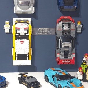 Puede incluir: Una colecci&oacute;n de coches de juguete, incluyendo un Audi e-tron rojo y gris, un Ford Mustang azul y naranja, un Audi Quattro gris y un Audi R8 blanco y amarillo. Los coches se muestran sobre un fondo azul con la palabra "quattro" impresa en blanco.