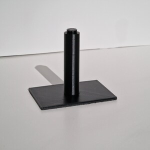May include: A black plastic stand with a cylindrical post and a rectangular base.