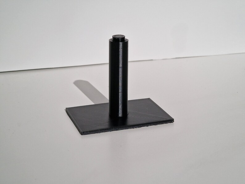 May include: A black plastic stand with a cylindrical post and a rectangular base.
