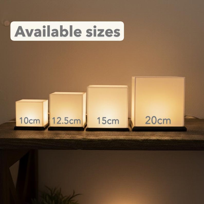 May include: Four square, glowing lamps of varying sizes are displayed on a wooden surface. The lamps are labeled with their sizes: 10cm, 12.5cm, 15cm, and 20cm. The text "Available sizes" is in a white rectangle above the lamps.