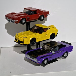 May include: Three toy cars stacked on a stand. The top car is red, the middle car is yellow, and the bottom car is purple.
