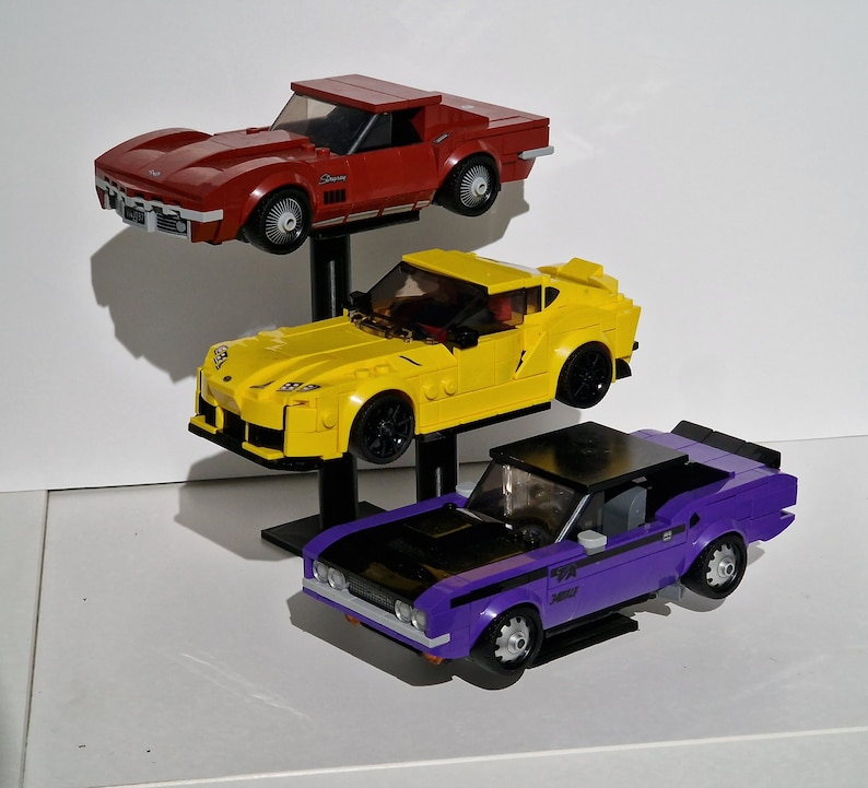 May include: Three toy cars stacked on a stand. The top car is red, the middle car is yellow, and the bottom car is purple.