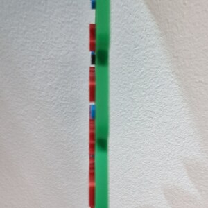Puede incluir: Un objeto rectangular verde con detalles rojos, negros y azules. El objeto tiene una parte superior roja y est&aacute; sobre un fondo blanco. El dise&ntilde;o es simple y moderno, con un enfoque en el color y la forma.