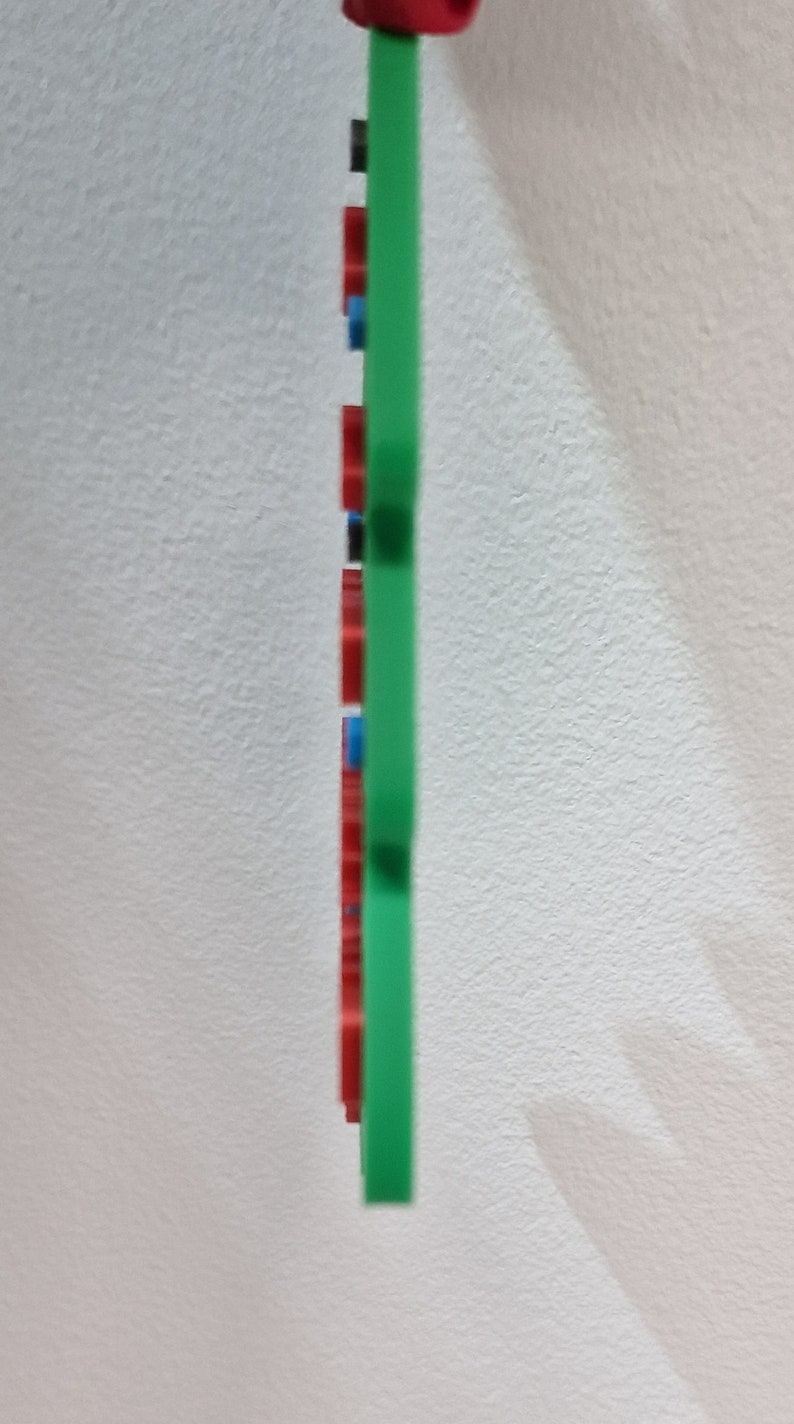 Puede incluir: Un objeto rectangular verde con detalles rojos, negros y azules. El objeto tiene una parte superior roja y est&aacute; sobre un fondo blanco. El dise&ntilde;o es simple y moderno, con un enfoque en el color y la forma.