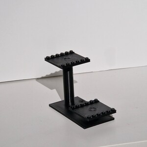 Op de afbeelding: Een zwarte plastic standaard met twee niveaus, gemaakt van Lego-stenen.