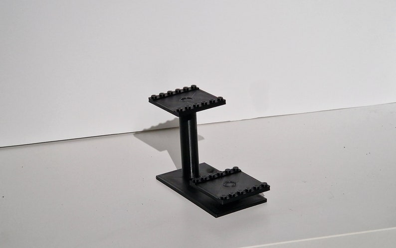 Op de afbeelding: Een zwarte plastic standaard met twee niveaus, gemaakt van Lego-stenen.
