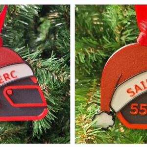 Op de afbeelding: Kerstboomversiering in de vorm van een racehelm, met een rood kerstmutsontwerp. De ornamenten tonen de naam "LECLERC" en het nummer "16". Een rood lint is bevestigd om op te hangen.
