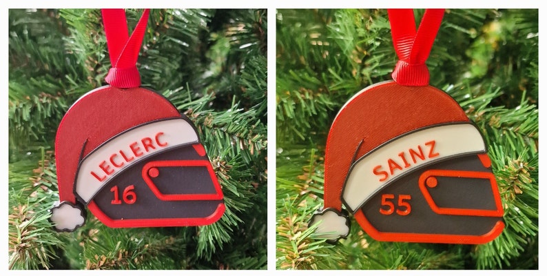 Op de afbeelding: Kerstboomversiering in de vorm van een racehelm, met een rood kerstmutsontwerp. De ornamenten tonen de naam "LECLERC" en het nummer "16". Een rood lint is bevestigd om op te hangen.
