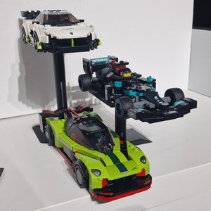 May include: Three toy race cars on display stands. A white and green car is on the top stand, a black and blue car with the word "PETRONAS" on the side is on the middle stand, and a green and black car is on the bottom stand.