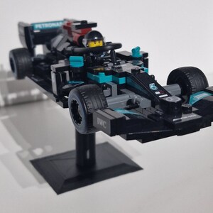 May include: A black and teal Lego Formula 1 race car with the number 6 on the side. The car is on a black stand and has the words "PETRONAS" and "IWC" printed on it.